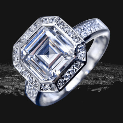Asscher Deco Ring featuring a large square-cut center stone surrounded by smaller stones, set in sterling silver with rhodium plating for a polished, elegant look.