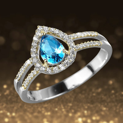 Dewdrop Halo Ring featuring a sterling silver band with a pear-shaped blue gemstone surrounded by a sparkling halo of small clear stones, designed for women’s jewelry.