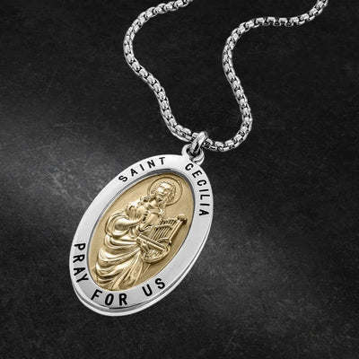 Stainless steel St Cecilia Pendant featuring a detailed gold-tone saint figure holding a harp, with the inscription "Saint Cecilia Pray For Us" on the oval medallion pendant.