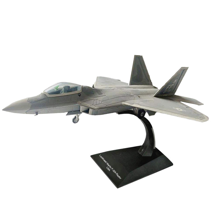 F-22A Raptor fighter jet model displayed on a black stand with twin tail fins, cockpit canopy, swept wings, and detailed gray military styling