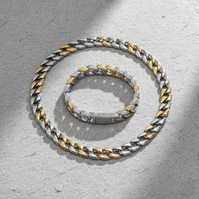 Two silver and gold chain necklaces on a textured gray surface.  Curb Vine Men's Set by Daniel Steiger