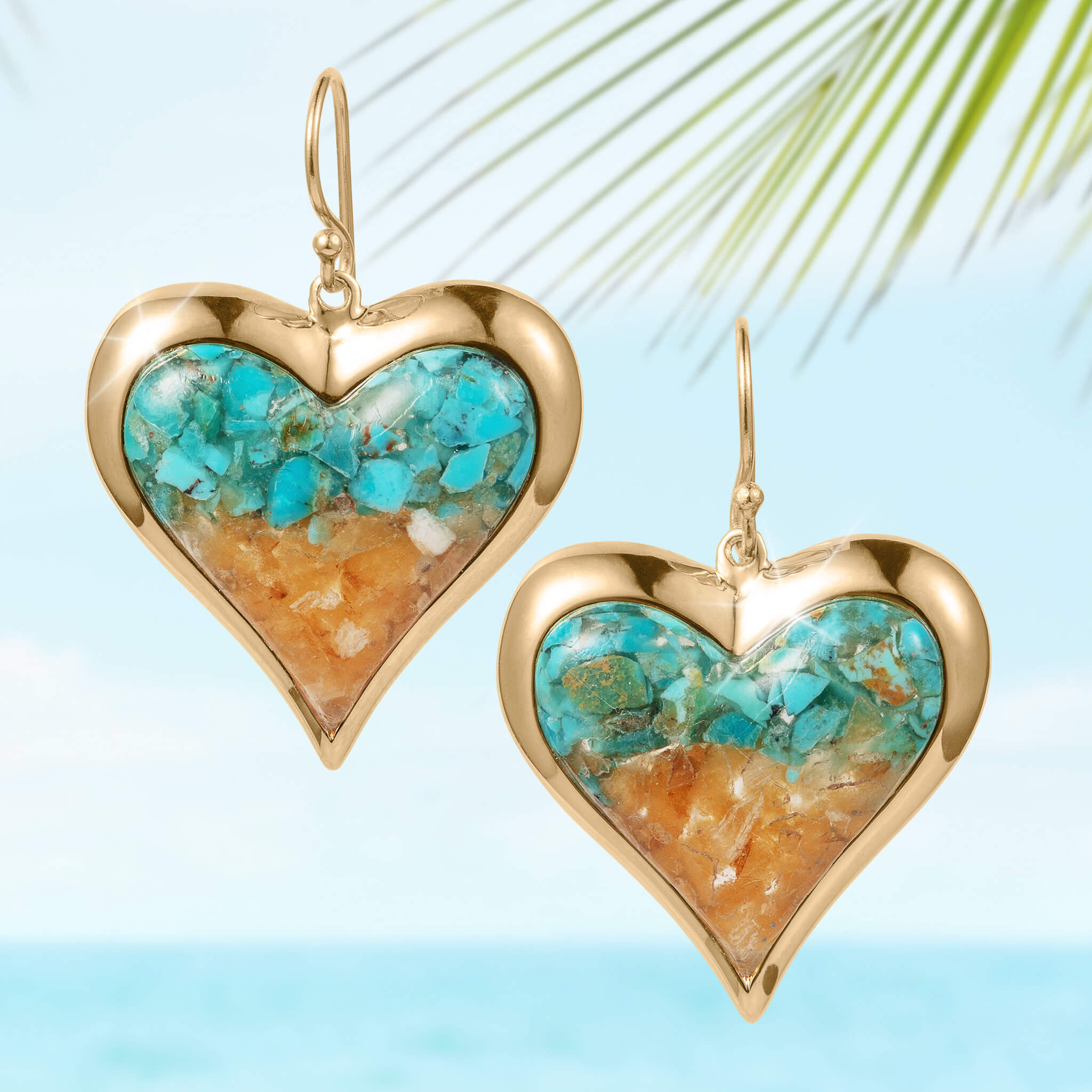 Sunlit Shore Heart Earrings featuring a gold heart-shaped frame with colorful turquoise and sandy beige stone inlay, hanging elegantly against a tropical backdrop.