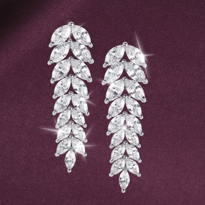 Long silver tone drop earrings with cascading marquise shaped crystal stones arranged in a leaf inspired design against a burgundy background