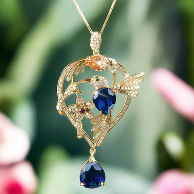 Golden Hummingbirds Pendant in sterling silver with gold plating, featuring intricate hummingbird design with blue and orange gemstones and sparkling accents on a delicate chain.