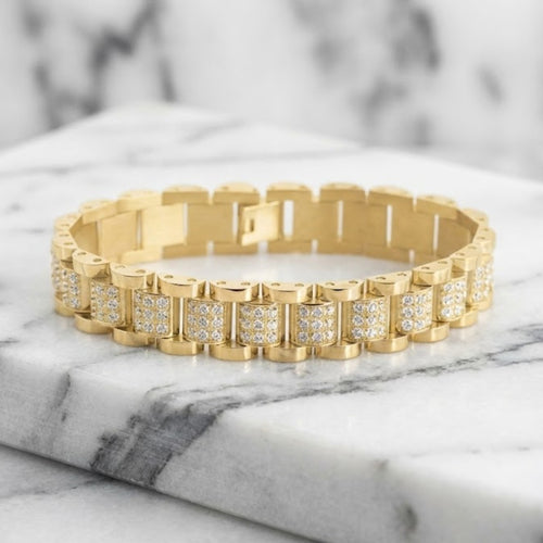 Gold bracelet with diamond accents on a marble surface. Daniel Steiger Marcos Men&