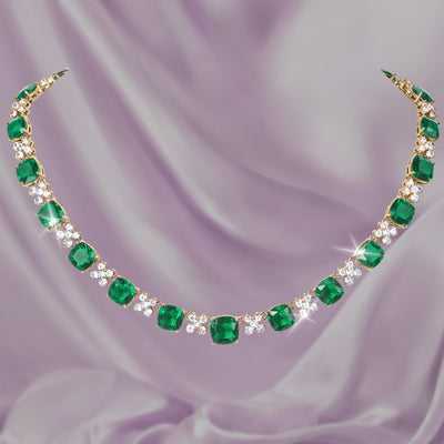 Freya Necklace with vibrant emerald green gemstones clear crystal accents and a gold tone setting displayed on soft lavender fabric Up To 75% Off Retail