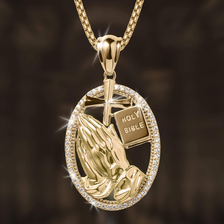 Holy Pendant featuring a gold-tone oval frame with sparkling stones, containing praying hands, a cross, and a Holy Bible design on a matching chain necklace.