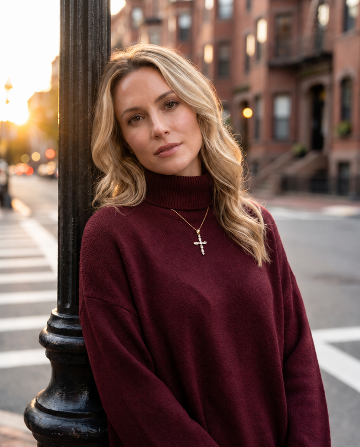 Celestial Light Cross Pendant worn by a woman in a burgundy sweater on a city street with a delicate cross necklace visible