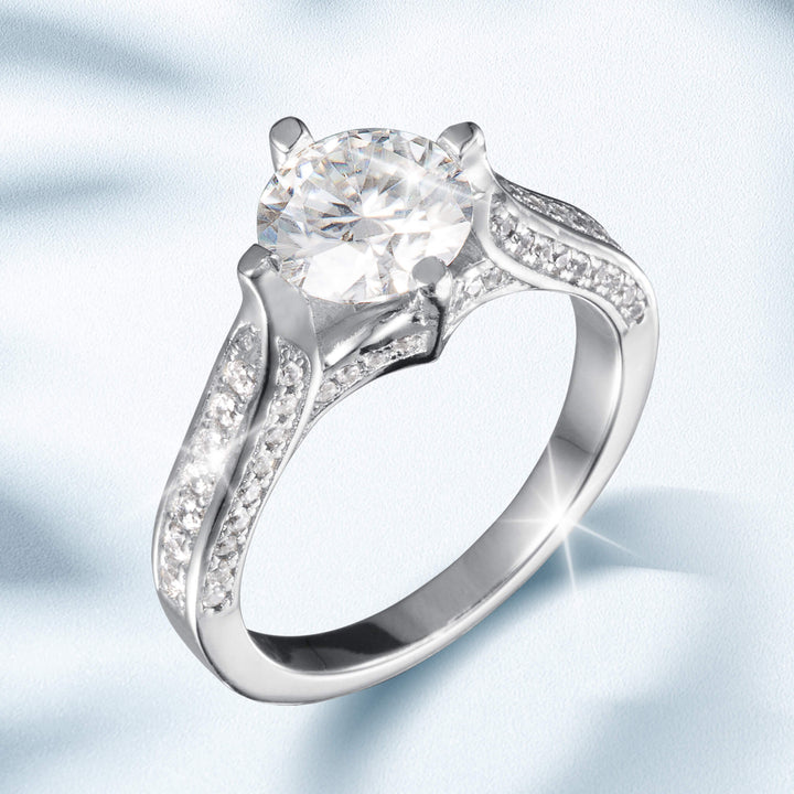 Novalyn Moissanite Ring featuring a large round center stone with a split shank band adorned with smaller sparkling accents in polished silver-tone metal.