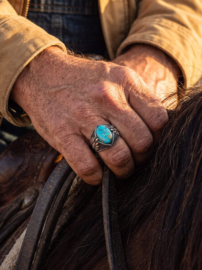 Turquoise Storm Men's Ring featuring a vivid turquoise stone and ornate silver detailing worn on a hand holding dark horse reins Up To 75% Off Retail