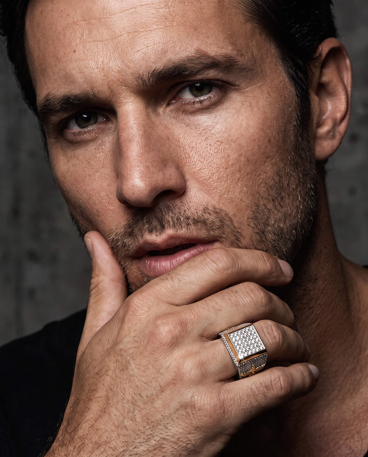 The Conqueror Ring worn on a mans hand in a close up portrait featuring a square pavé setting with sparkling stones and a dark center detail