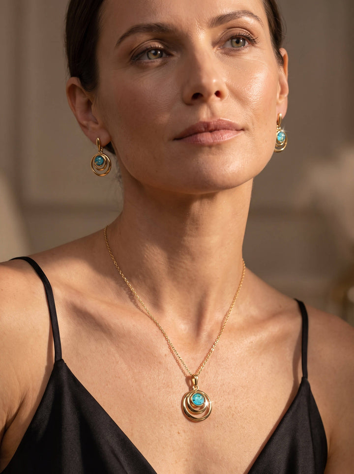 Woman wearing a black camisole with a gold pendant necklace and matching turquoise earrings in a softly lit indoor setting