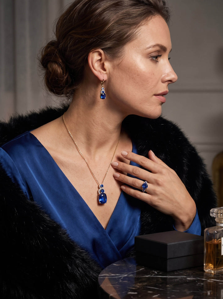 Elara Sapphire Earrings with blue sapphire drop stones styled on a woman in a satin blue dress and black fur wrap