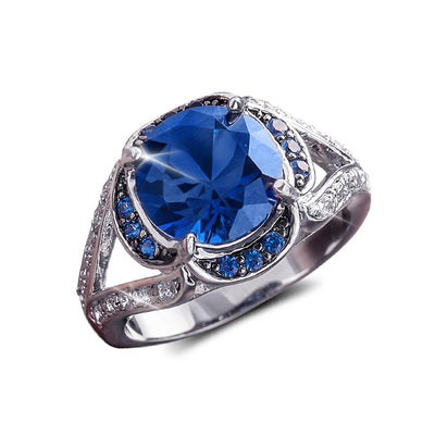 Electra Ring featuring a large blue gemstone centerpiece, set in sterling silver with rhodium plating, accented by smaller blue and clear stones for an elegant female jewelry piece.