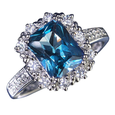 Marselles Ring featuring a large blue gemstone centerpiece surrounded by small clear stones, crafted in sterling silver with rhodium plating for a sophisticated women's jewelry piece.